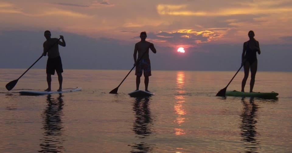 Three paddleboarders silhouetted at sunset on calm coastal water