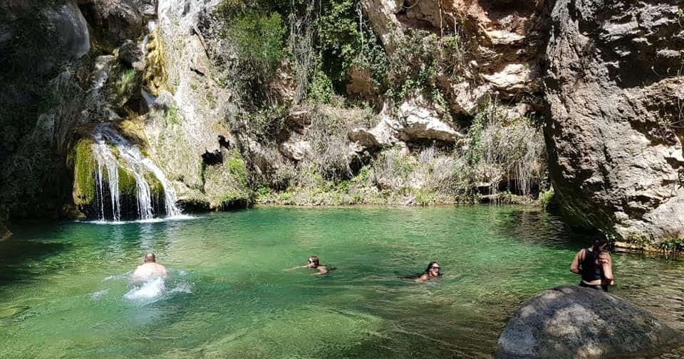 People swimming in emerald waterfall pool in rocky gorge