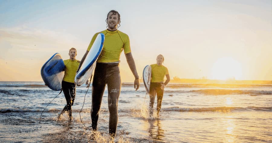 Surfers walking on sunset beach with surfboards