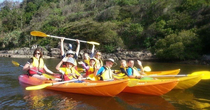 Large group kayaking in bright kayaks in a narrow river cove