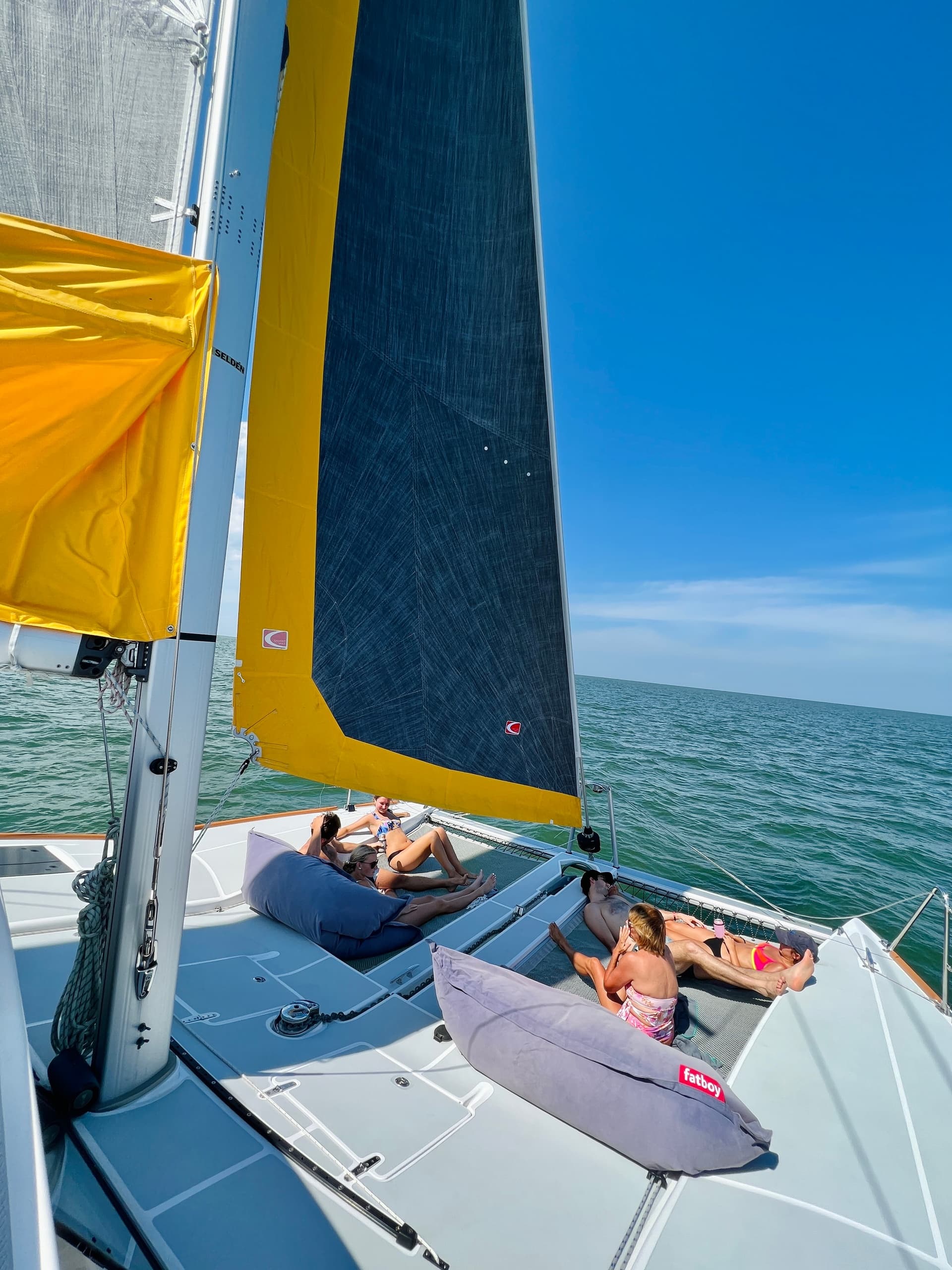 Sailors lounging on trimaran beneath large yellow sail in open sea