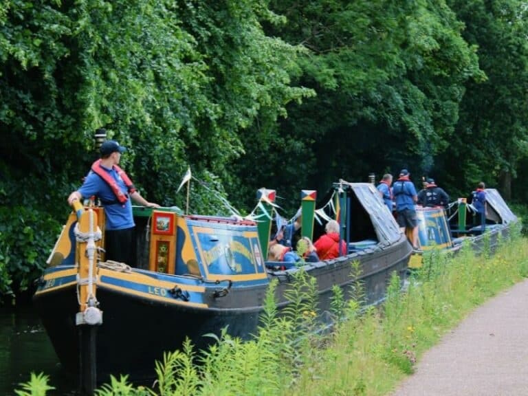 Family riding colorful narrowboat along leafy towpath canal