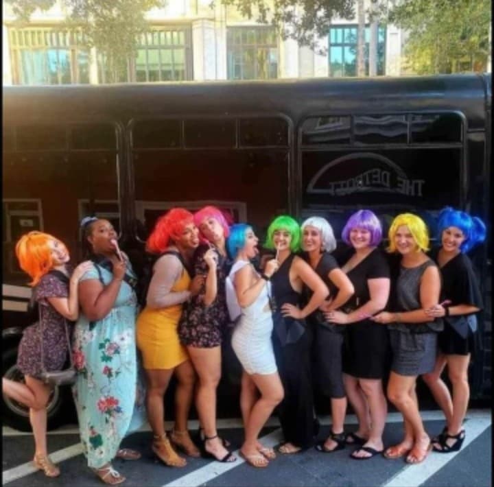 Group in colorful wigs posing by party bus on city street