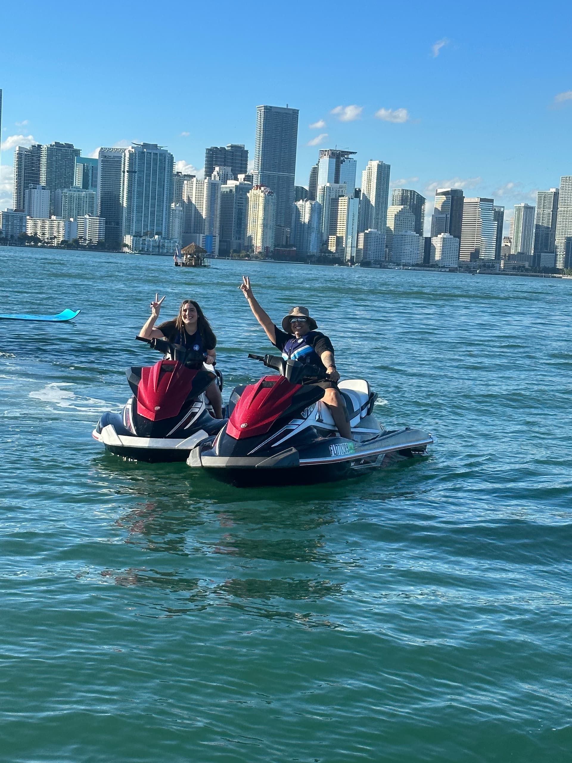 Two riders posing on red jet skis with Miami skyline behind