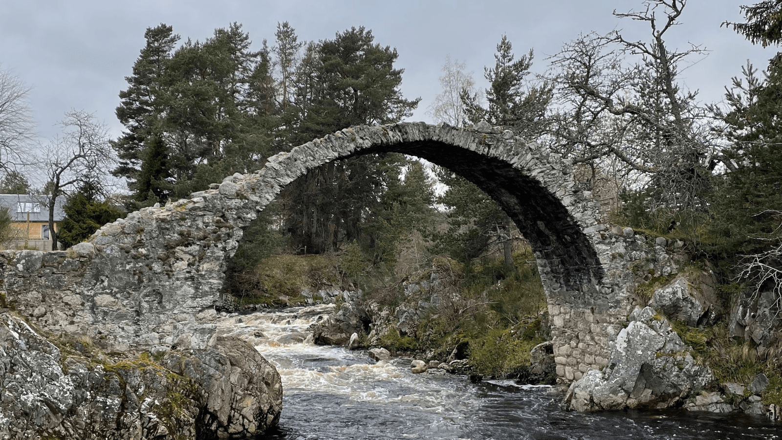 Ancient stone arch bridge over river in Scottish Highlands landscape
