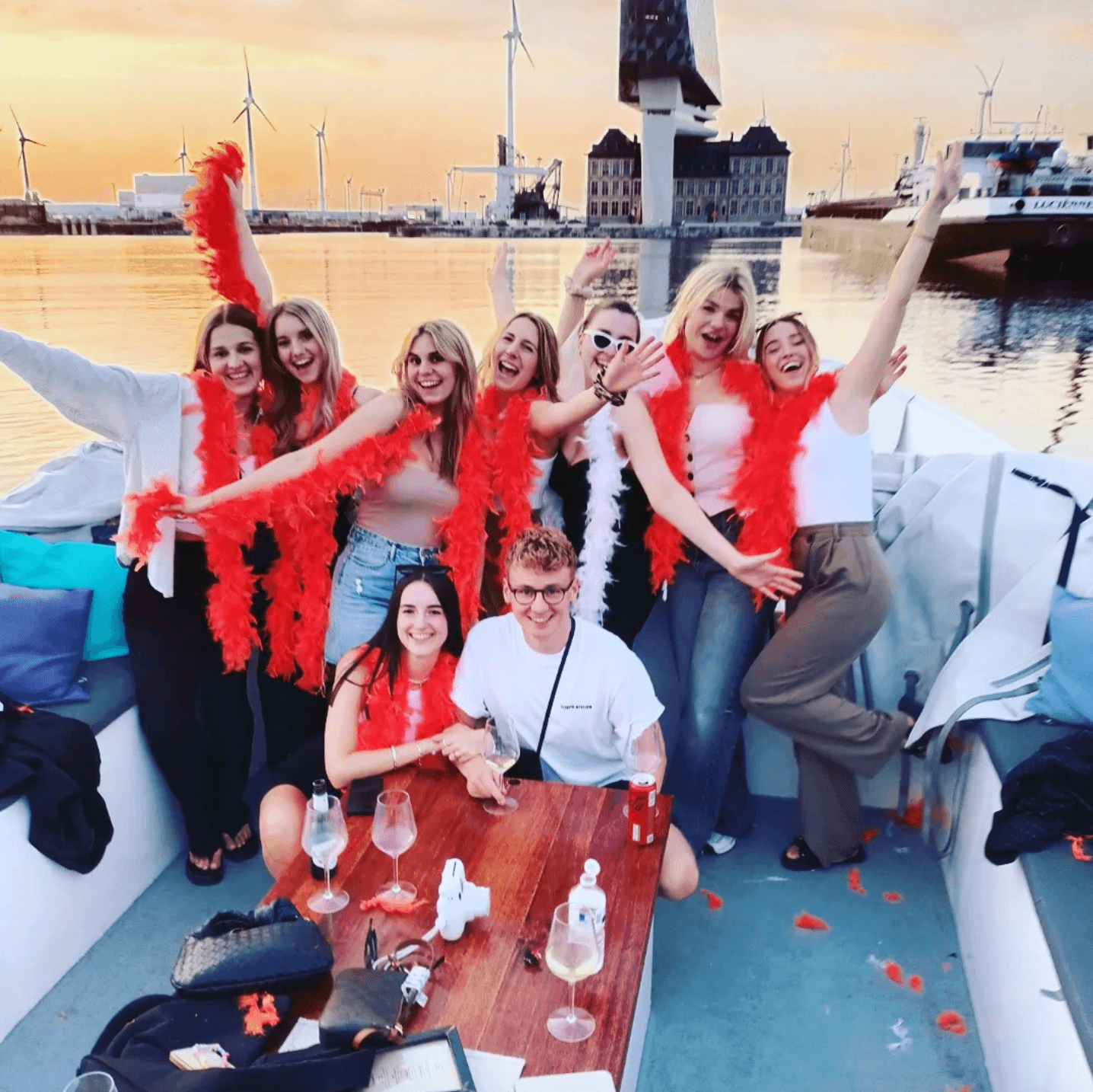 Group celebrating on sunset harbor boat with festive red boas
