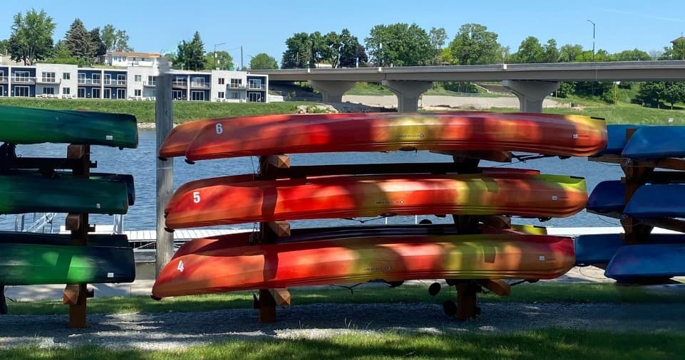 Colorful kayaks stacked on rack by riverside in sunny park