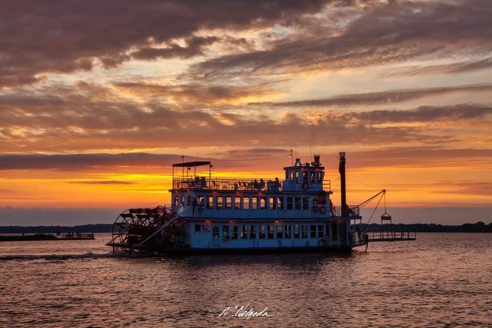 Sunset riverboat silhouette cruising on calm water, scenic harbor