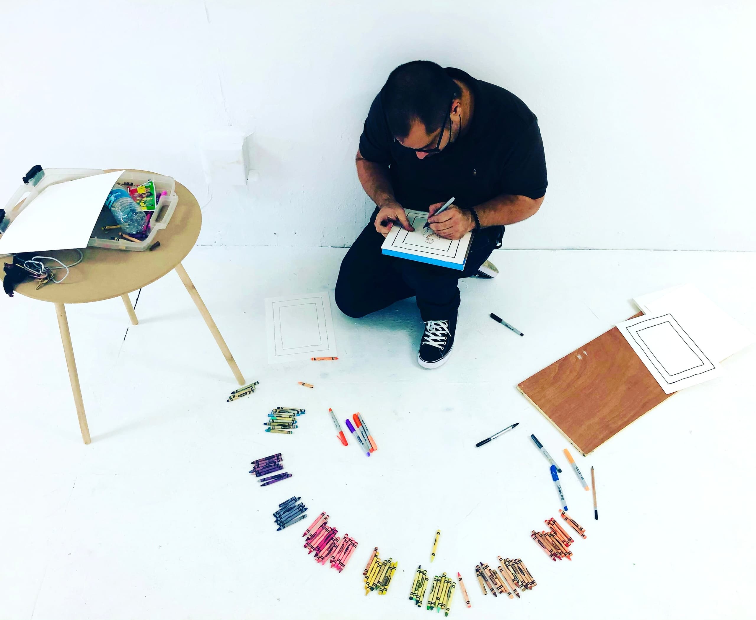 Artist sketching on studio floor surrounded by crayons and tools