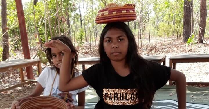 Young girl balancing woven basket in shaded bush learning space