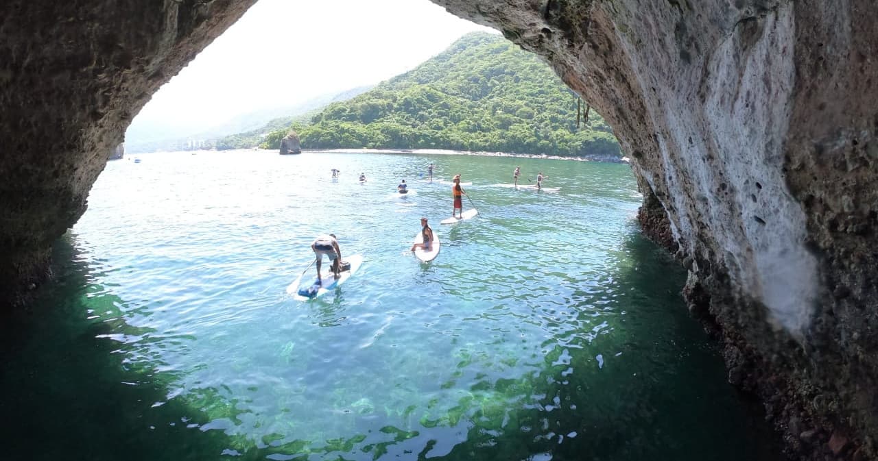 Paddleboarders exploring turquoise sea cave and coastal arch