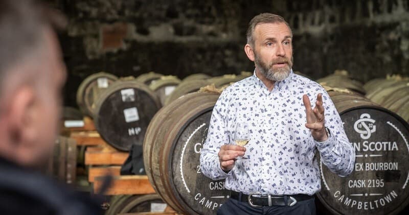 Distillery tour guide presenting whisky casks in warehouse