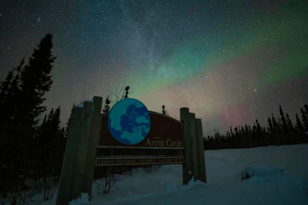 Arctic Circle sign under colorful aurora borealis at night