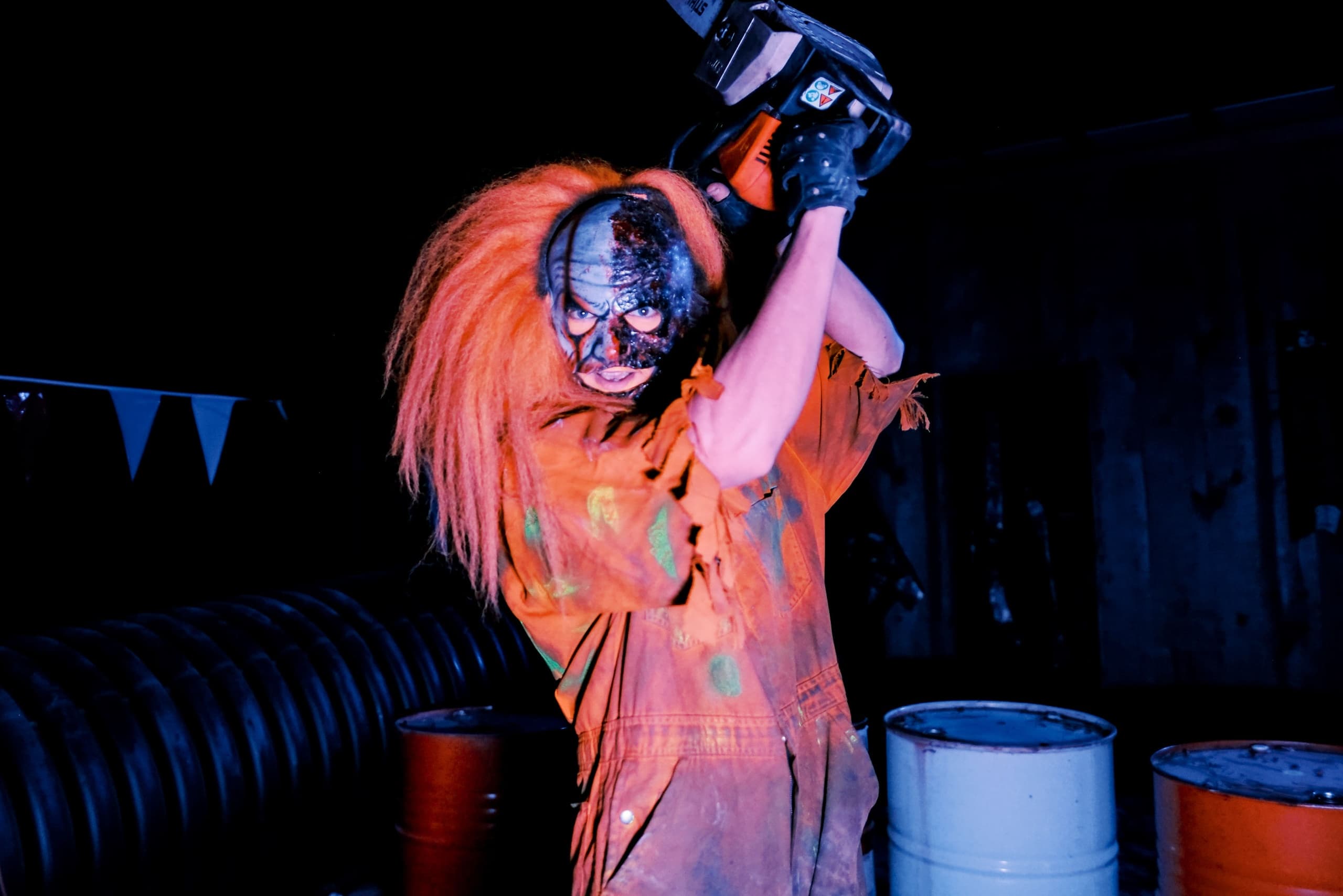 Masked performer wielding chainsaw at indoor haunted attraction