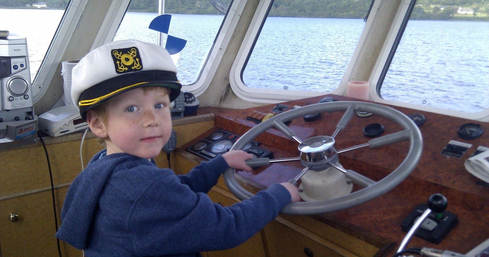 Child steering boat wheel inside pilothouse, family boating experience