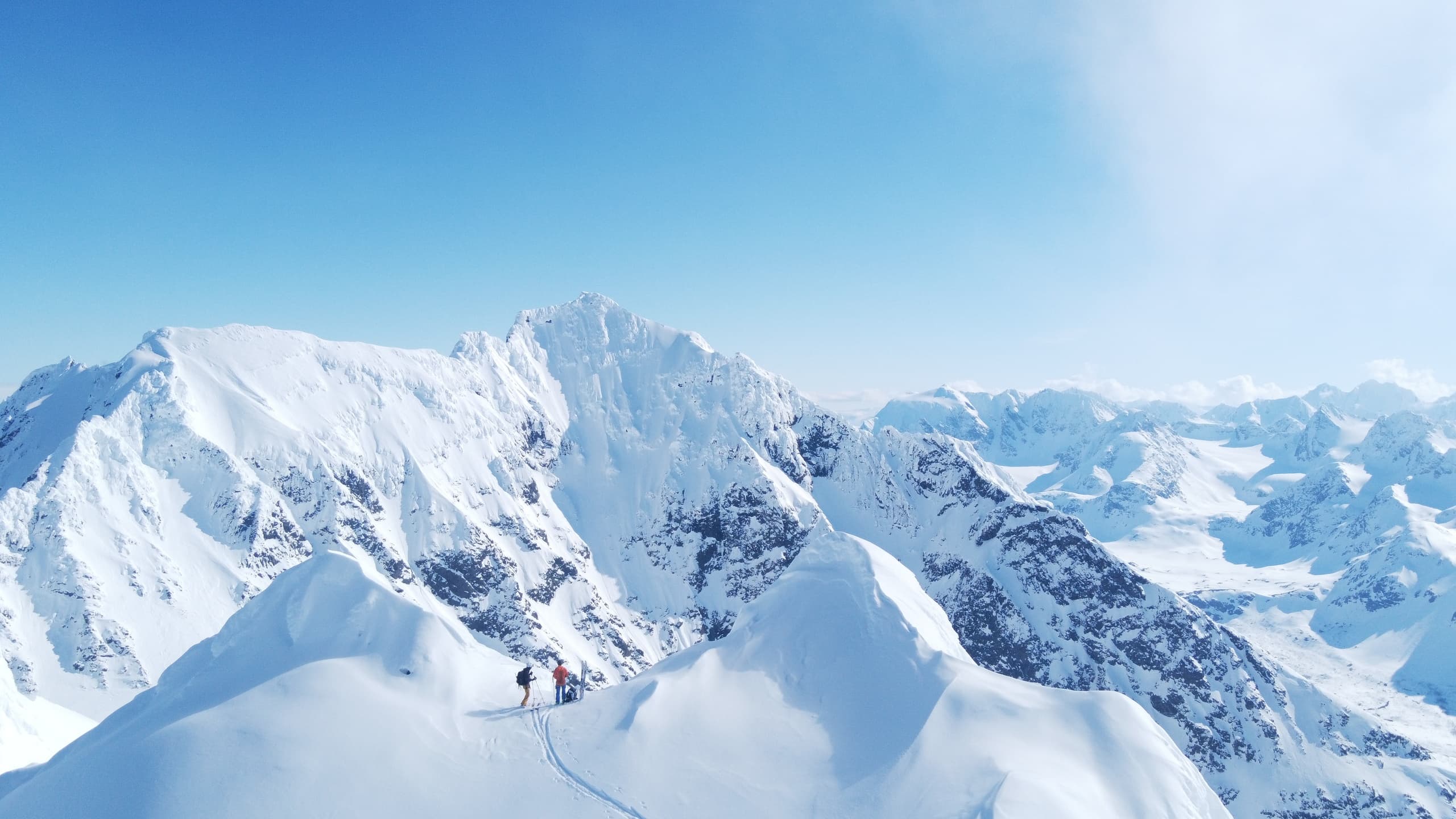 Skiers traversing snowy alpine ridge with panoramic mountain views