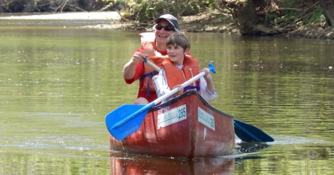 Parent and child paddling a red canoe on tranquil river