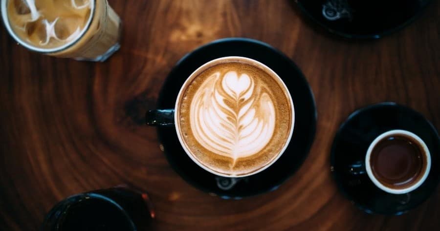 Latte art cappuccino on wooden table inside a Kona coffee shop