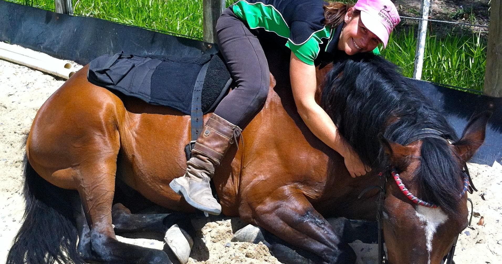 Rider embracing resting horse in outdoor sand arena, equine therapy