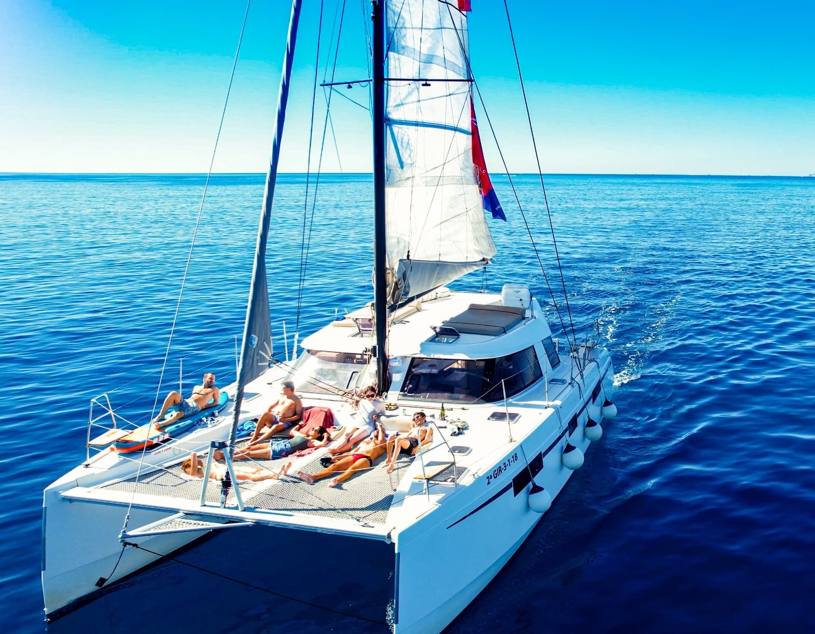 Catamaran with sunbathers on deck, calm Mediterranean waters