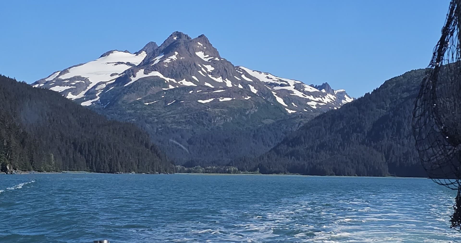 Snowy mountain peak above blue glacial lake, Alaska coast