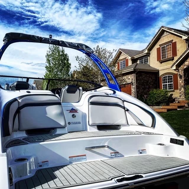 Blue and white wake boat parked with scenic sky and homes