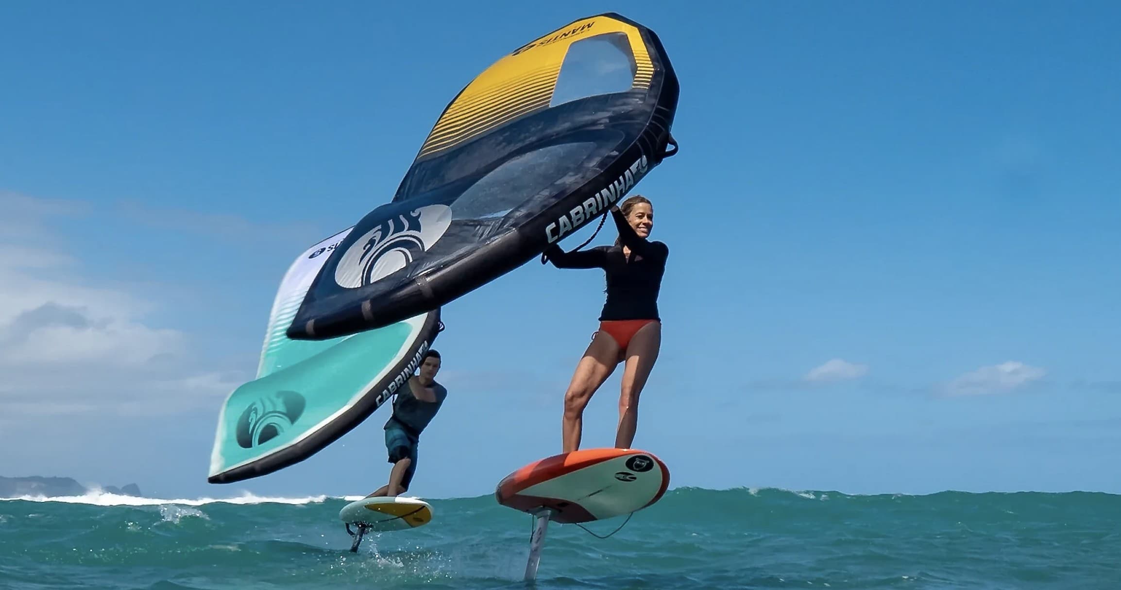 Two wingfoilers foiling above turquoise ocean waves in action