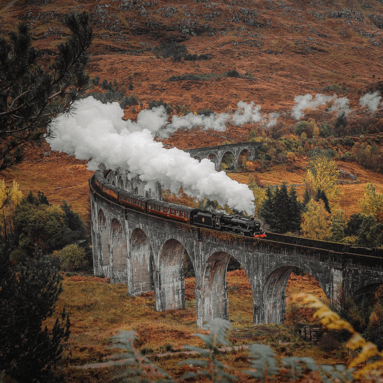 Steam train crossing iconic Glenfinnan viaduct, scenic ride