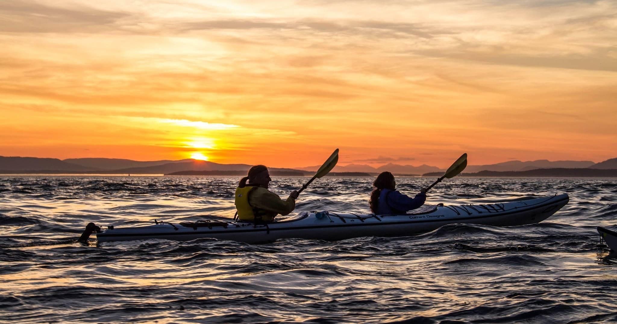 Two kayakers paddling at sunset offshore on open ocean near islands