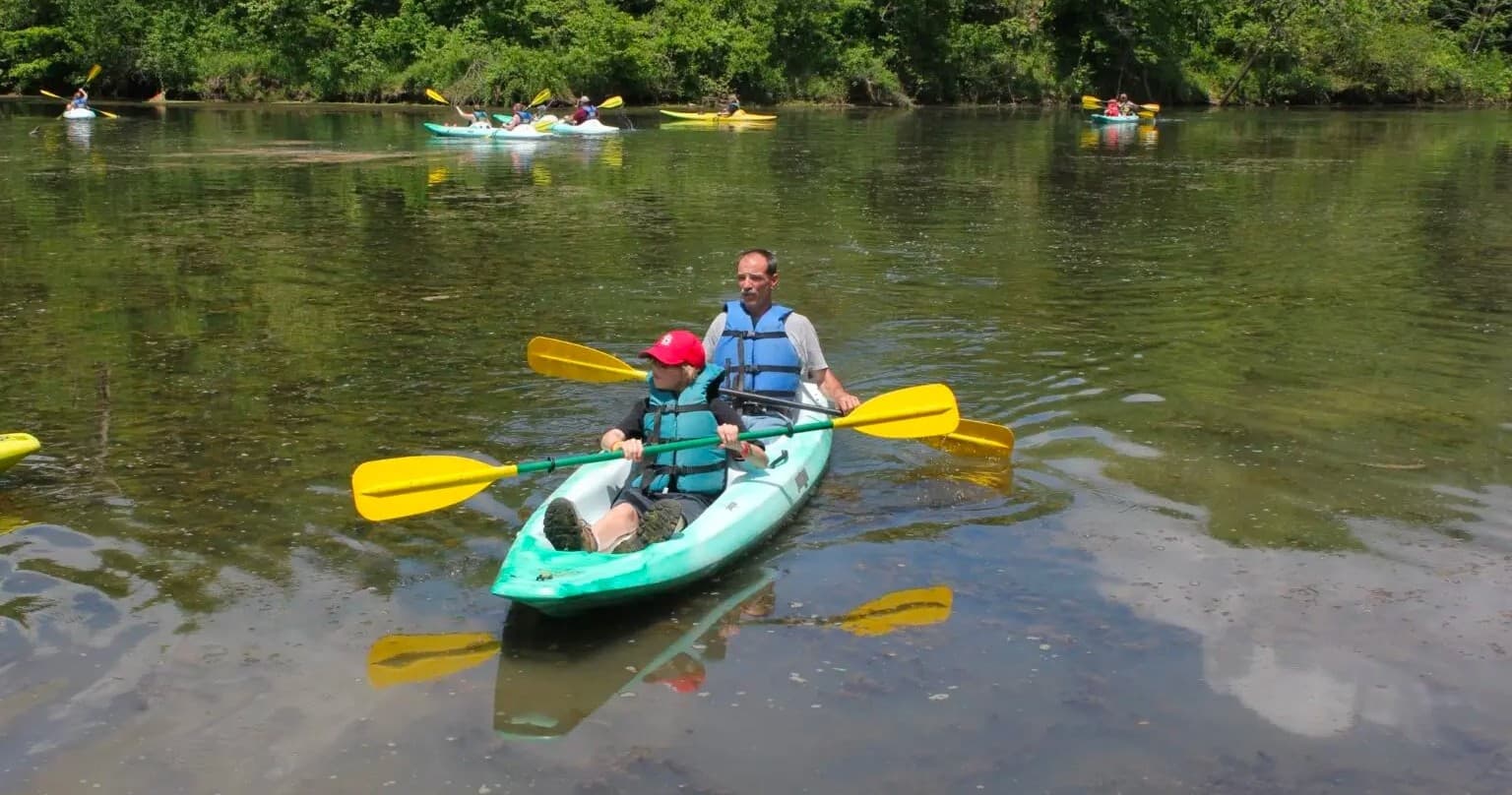 Two kayakers paddling tandem on shallow river with reflections