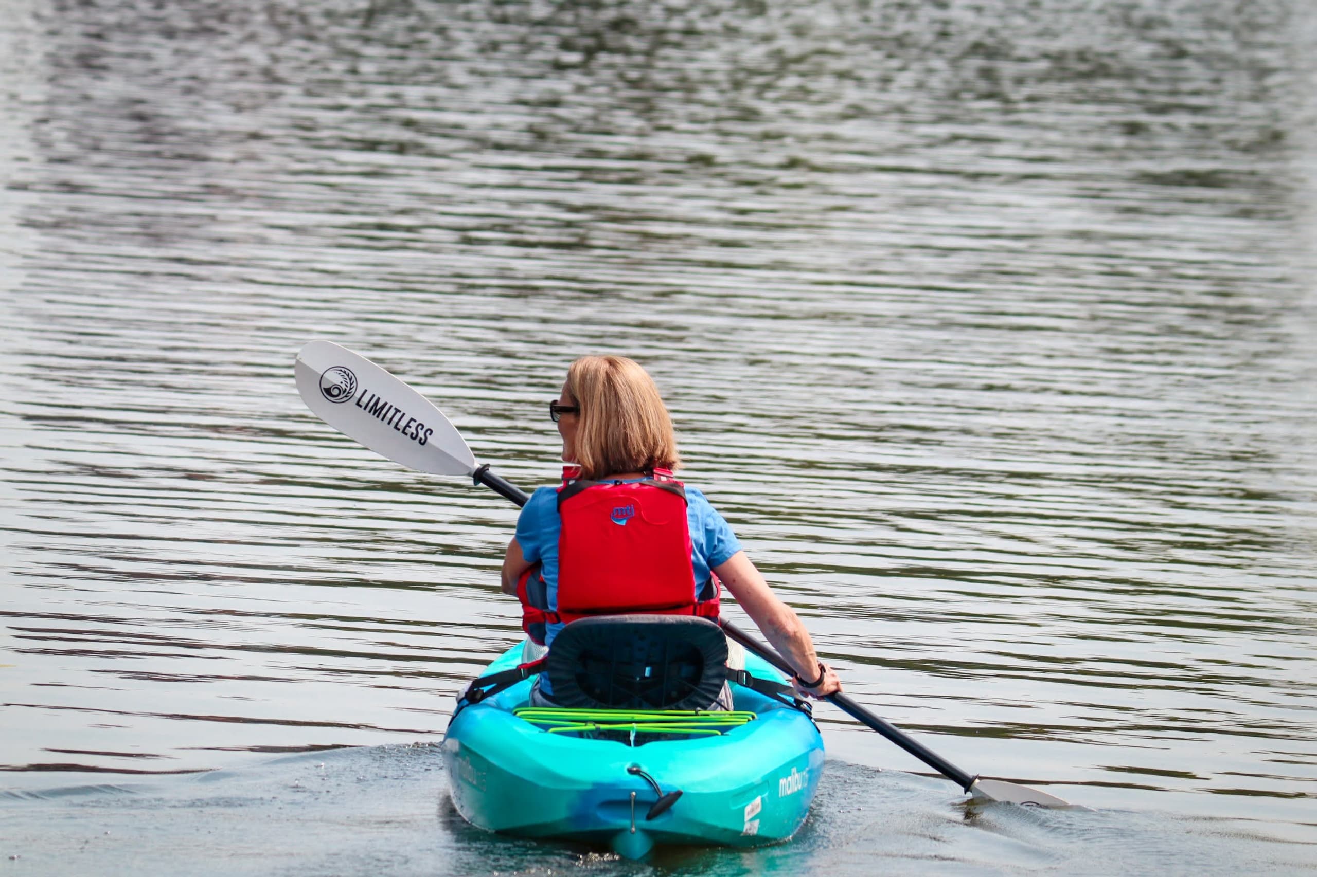 Solo kayaker paddling away on calm lake, rear view