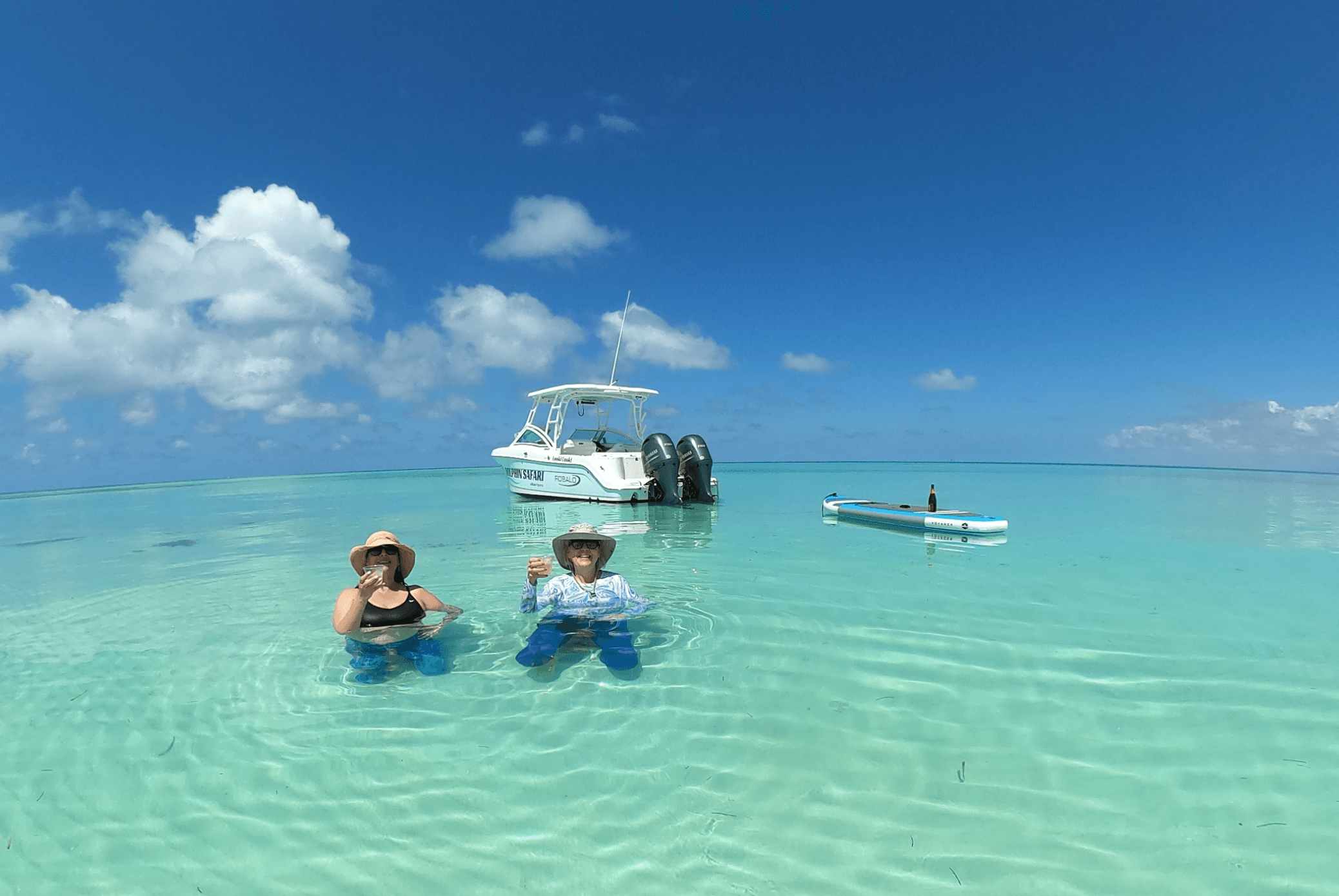 Tourists wading in turquoise shallow water with anchored boats