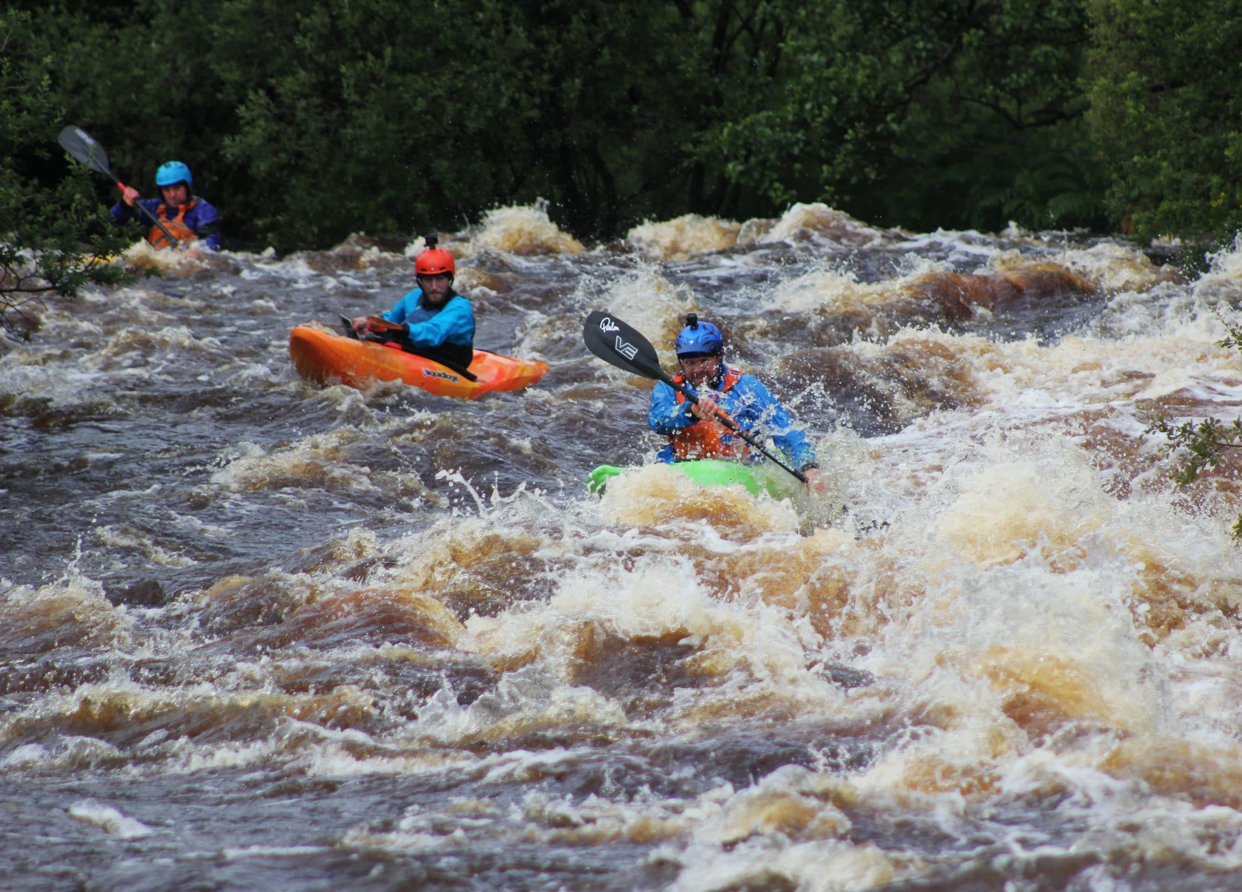 Whitewater kayakers navigating fast river rapids in forest