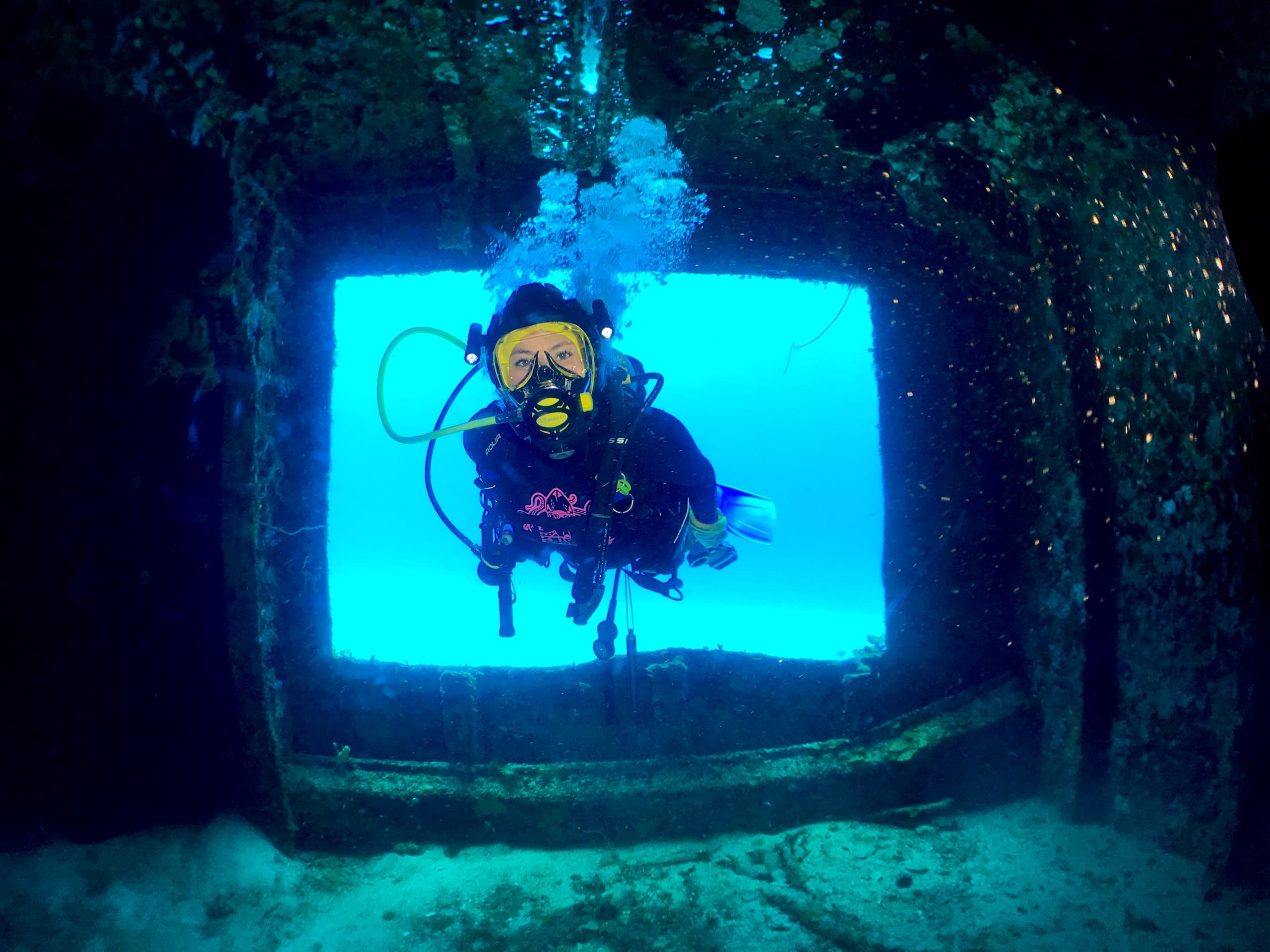 Scuba diver exploring sunlit wreck window off Cozumel reef