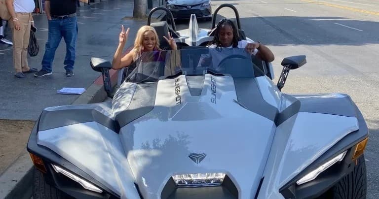 Two people driving silver Slingshot on urban street for sightseeing