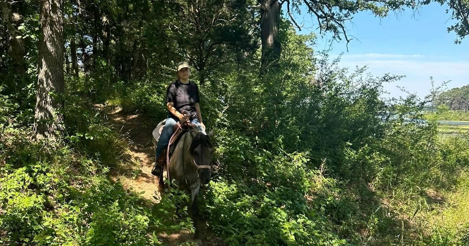 Rider navigating shaded forest trail on horseback near river