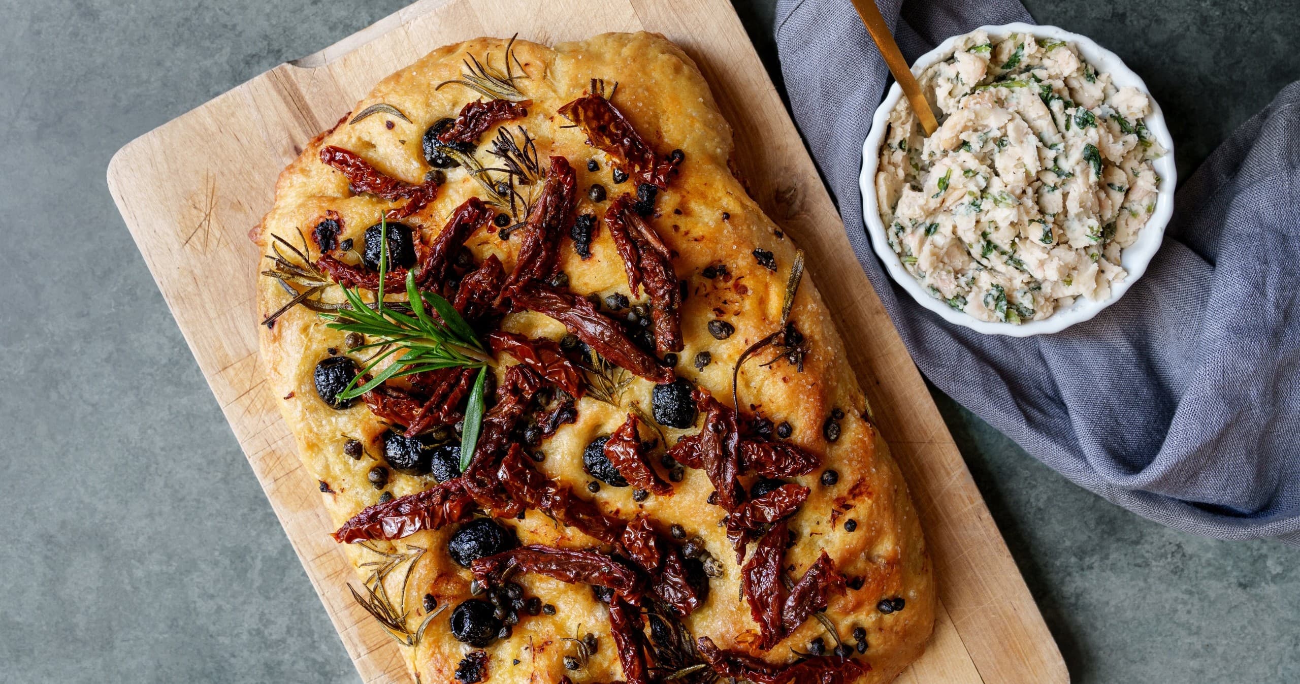 Woodboard sun-dried tomato focaccia with herb dip, rustic table