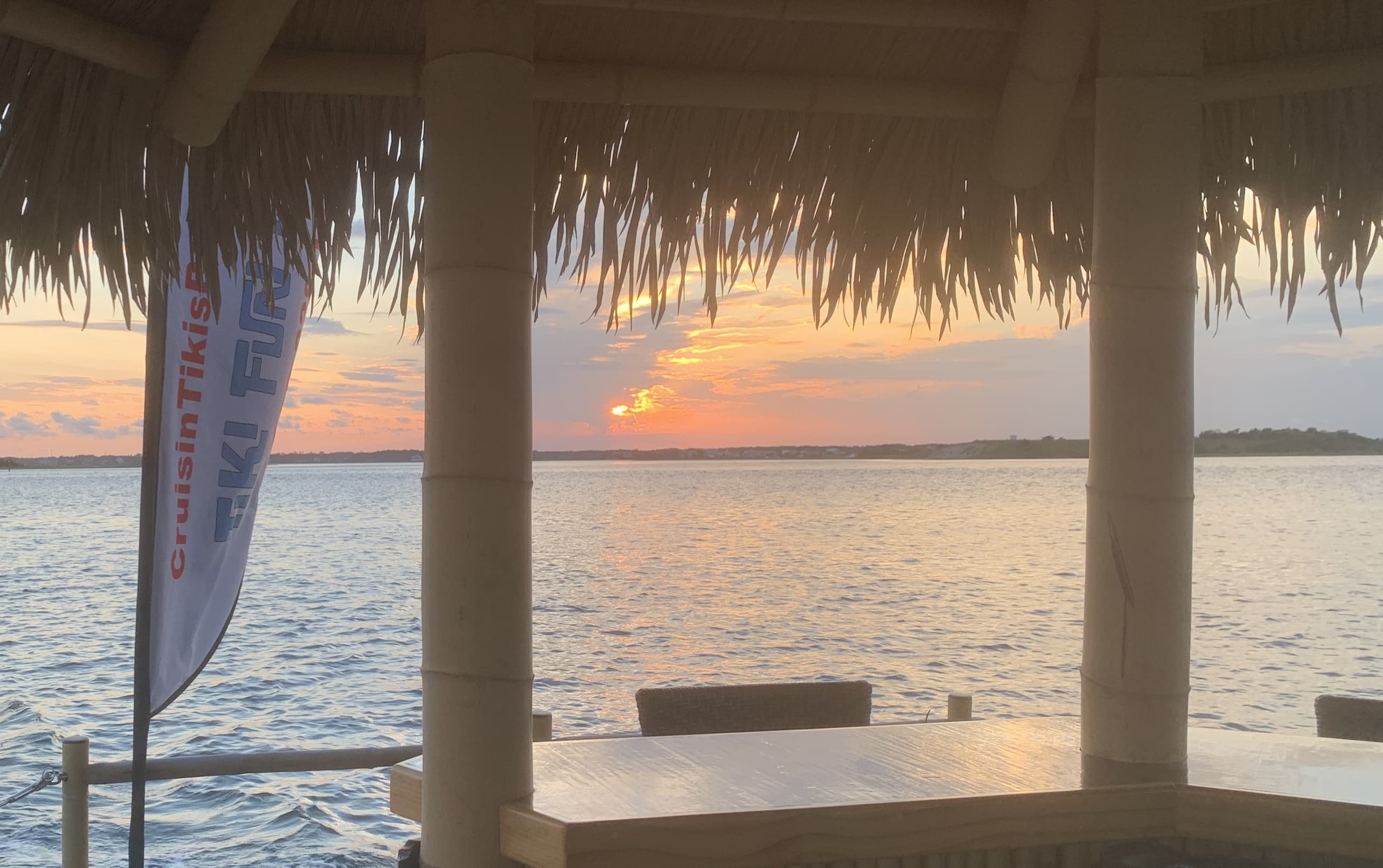 Golden sunset framed by tiki hut posts over tranquil coastal inlet