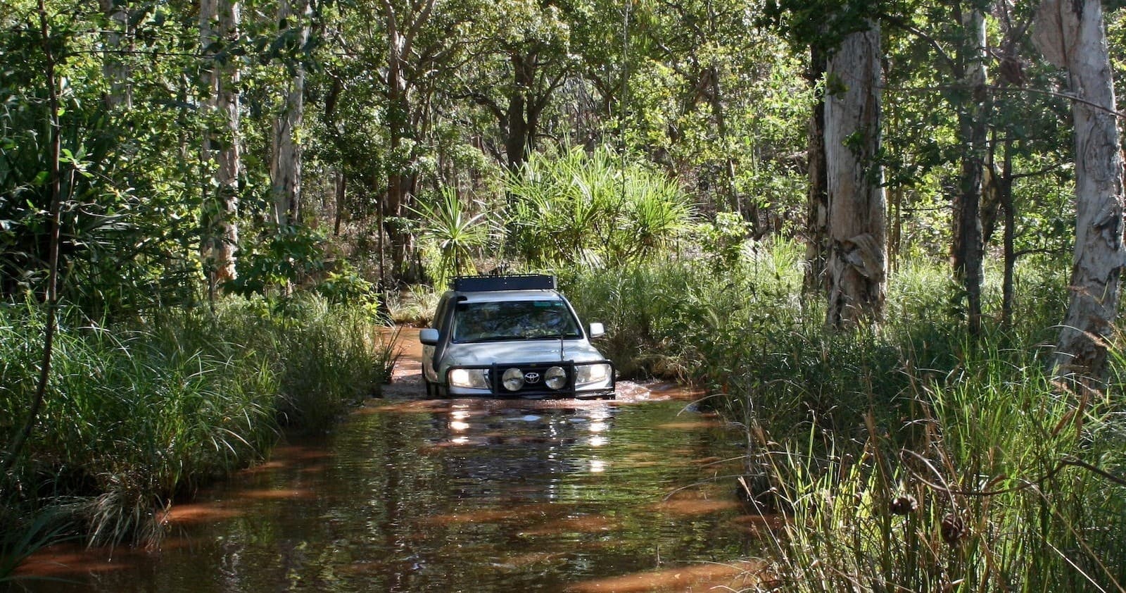 4x4 vehicle fording a flooded rainforest creek on outback track