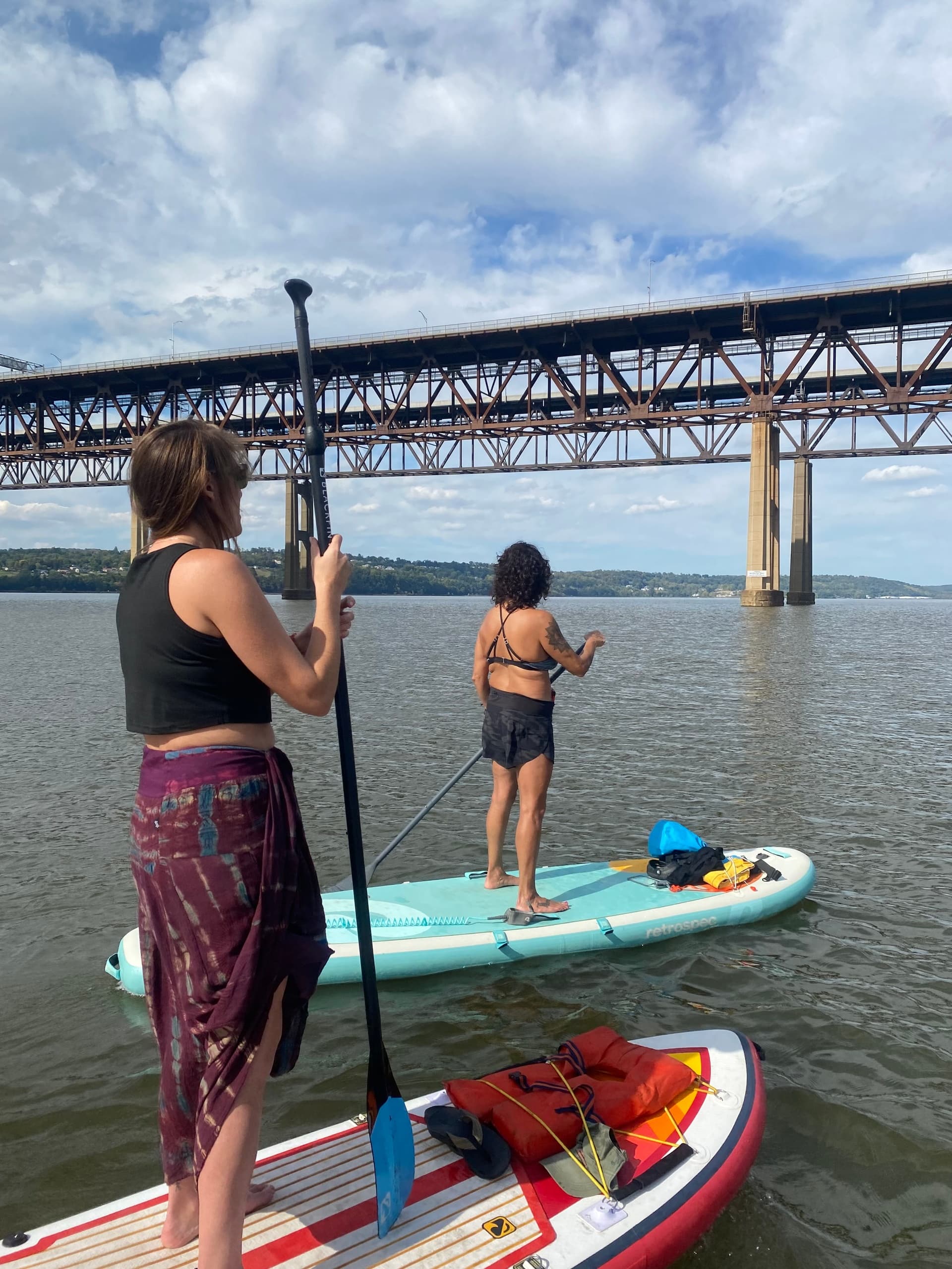 Stand-up paddleboarders paddling under large river bridge