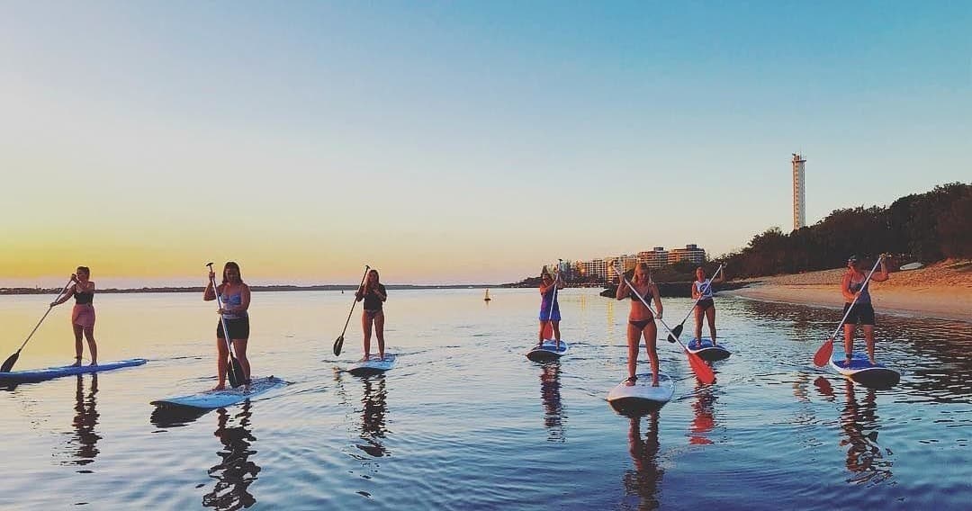 Group stand-up paddleboarding at sunset along coastal shore