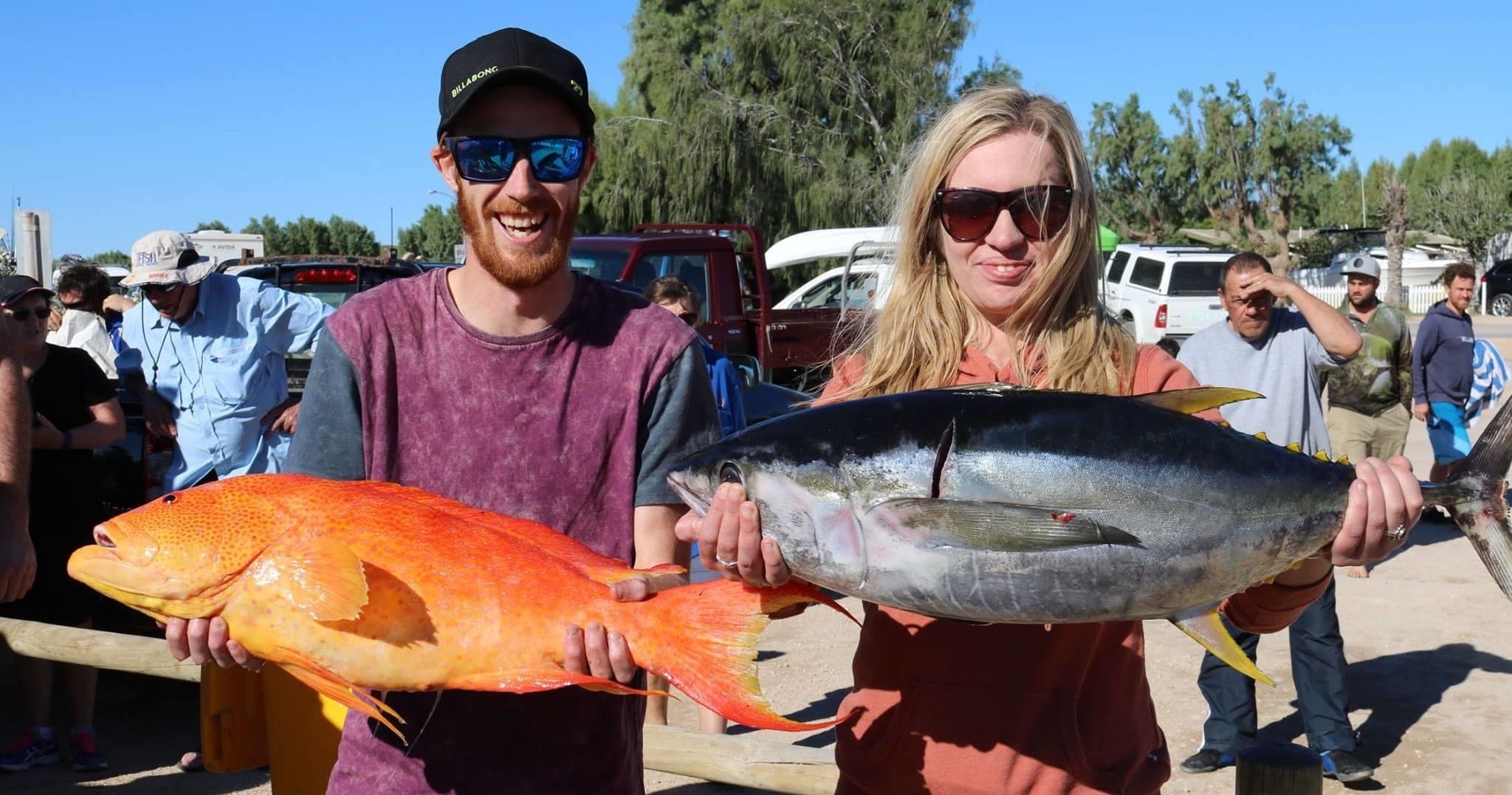 Two anglers displaying orange coral trout and tuna at dock