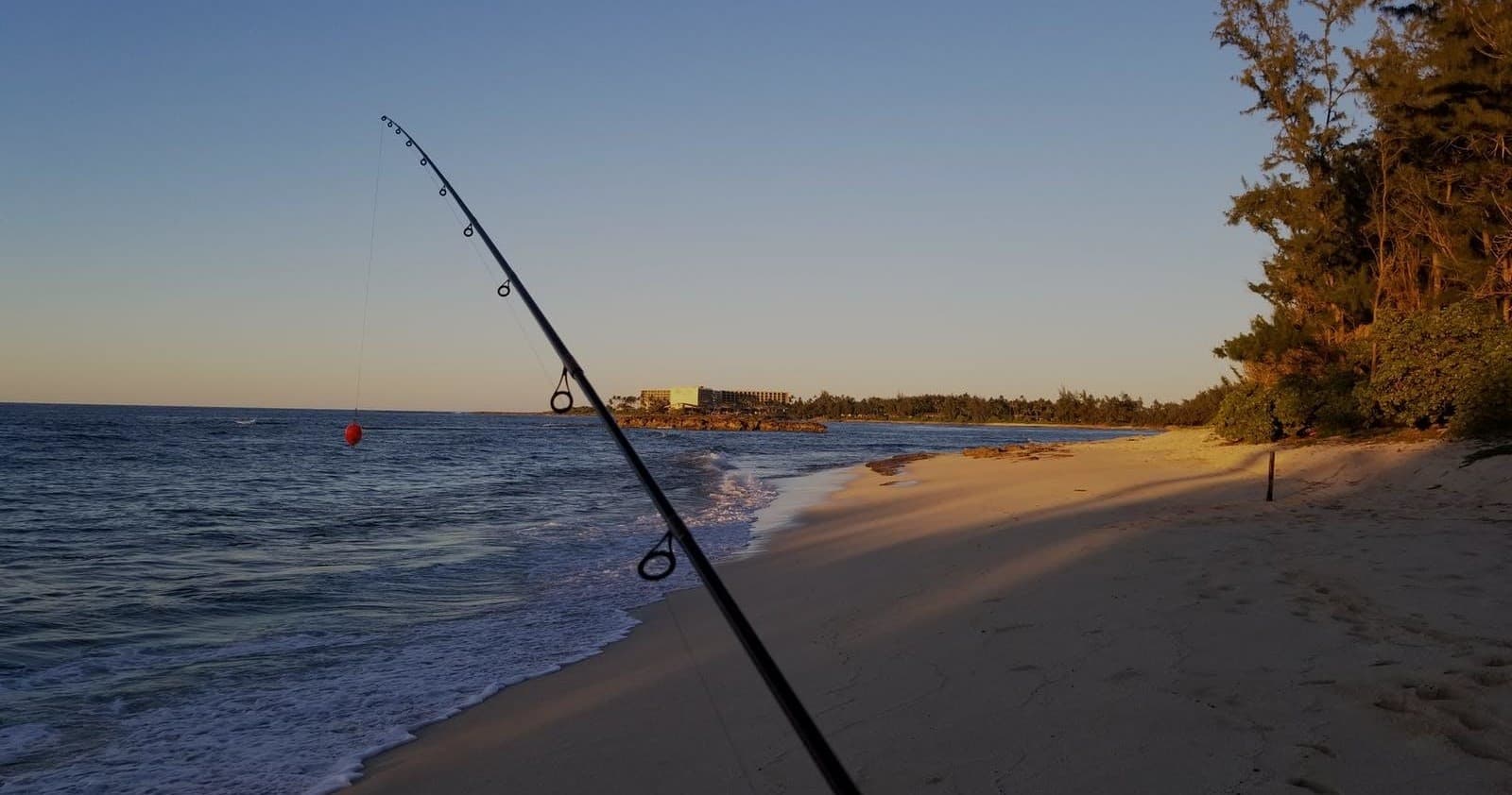 Shoreline fishing on Hawaiian beach at sunset with rod cast