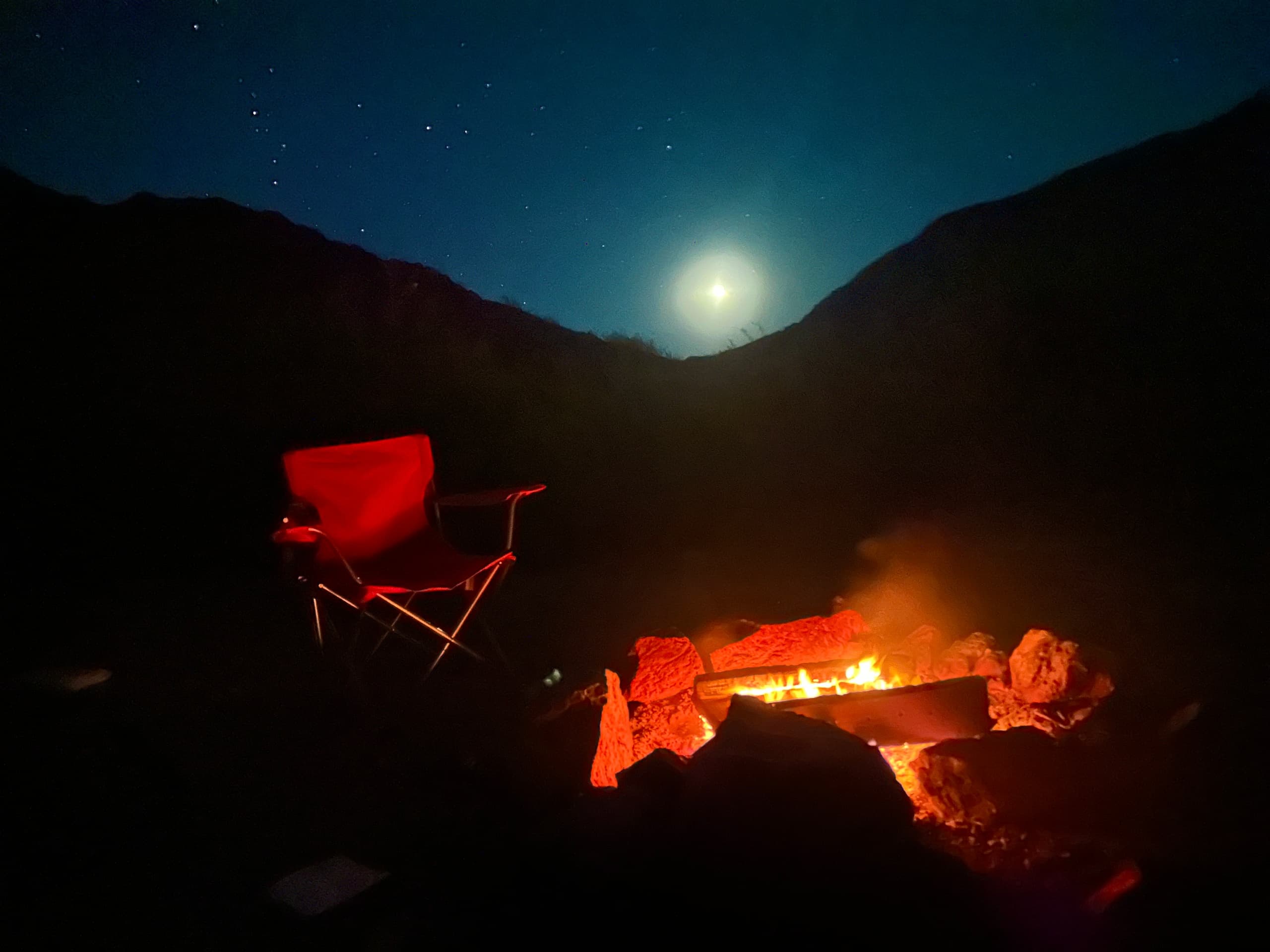 Night campsite with campfire under moonlit desert canyon