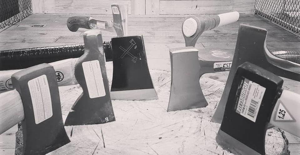 Axes lined up on wooden table inside indoor axe-throwing venue