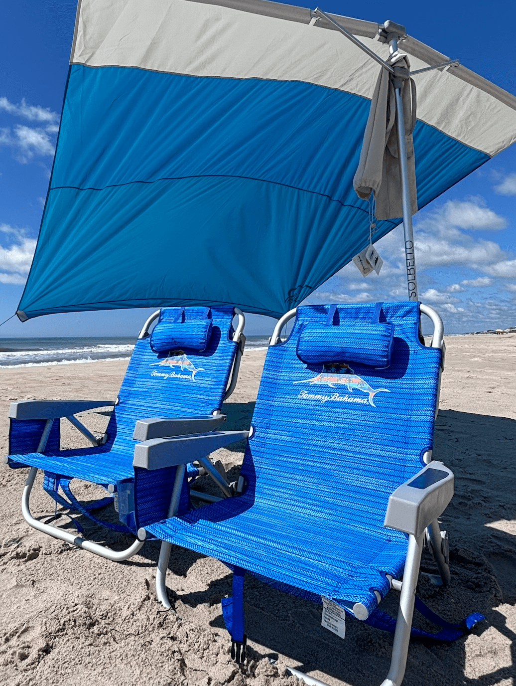 Two beach chairs under large sun canopy on sandy shoreline
