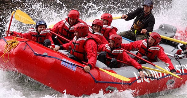 Guide-led red raft full of paddlers cresting big whitewater waves