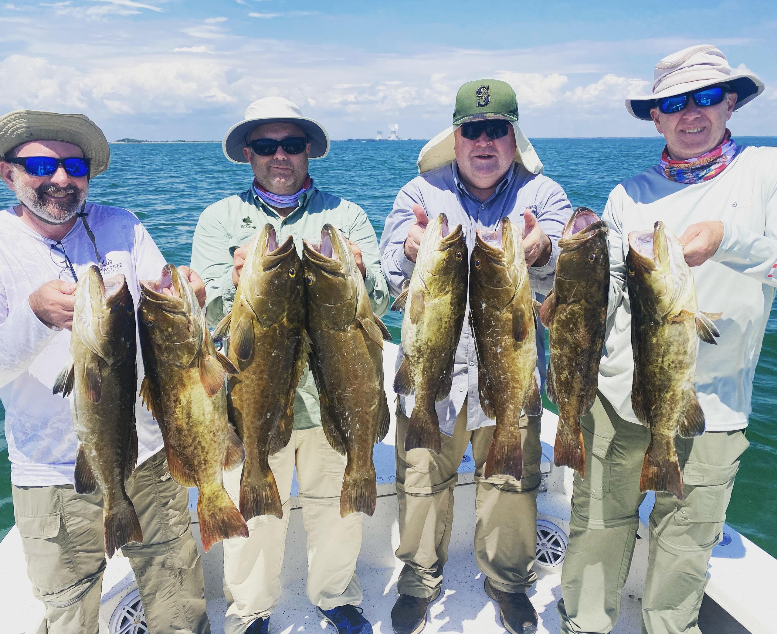 Four anglers displaying multiple grouper catch on Florida boat