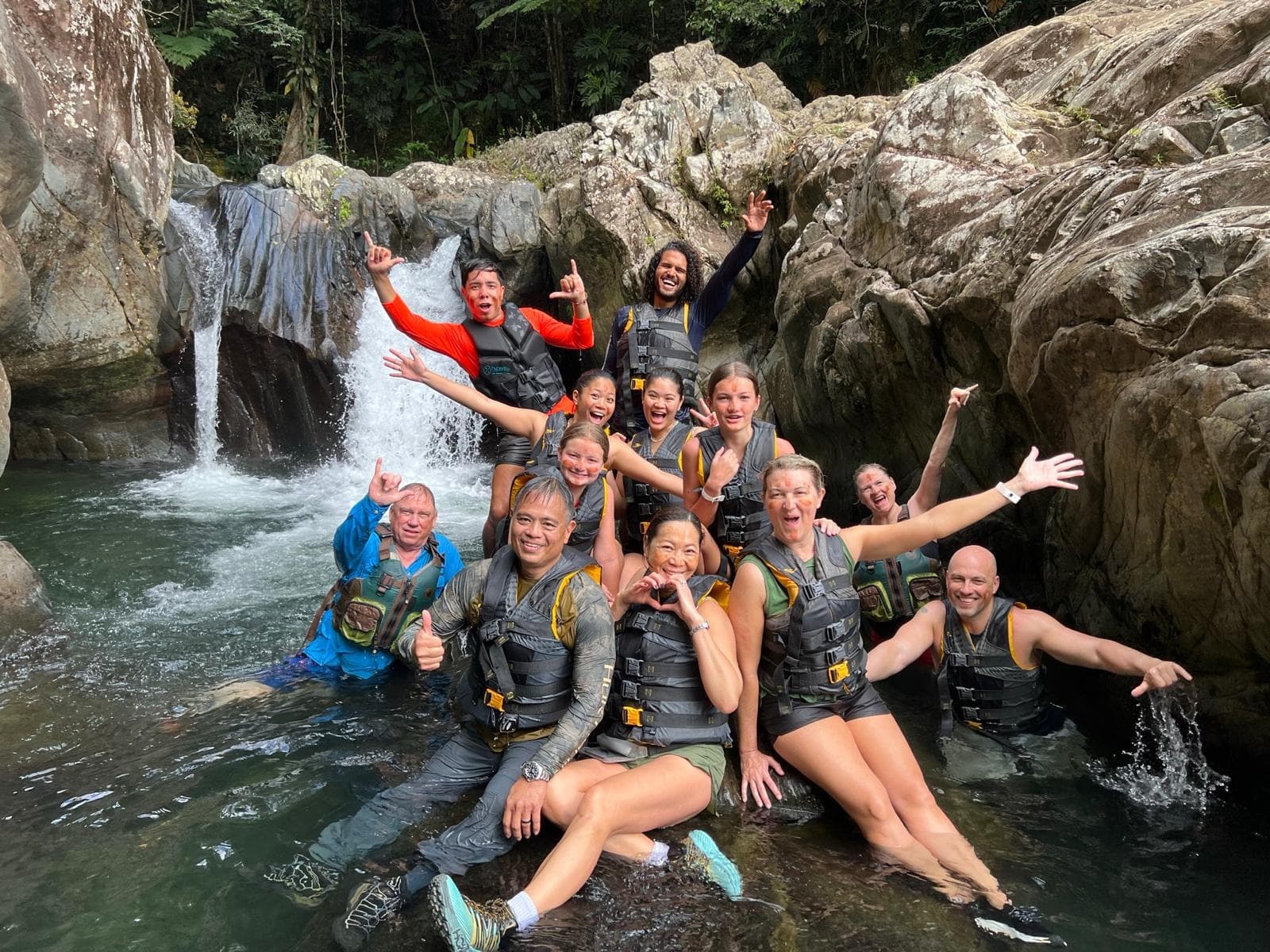 Group canyoning in rocky waterfall pool, tropical river adventure