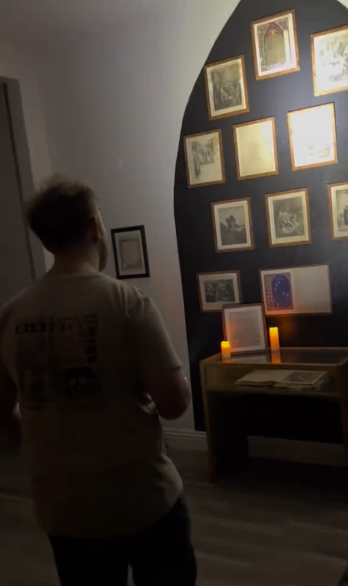 Visitor viewing framed photos in dim paranormal museum room with candles